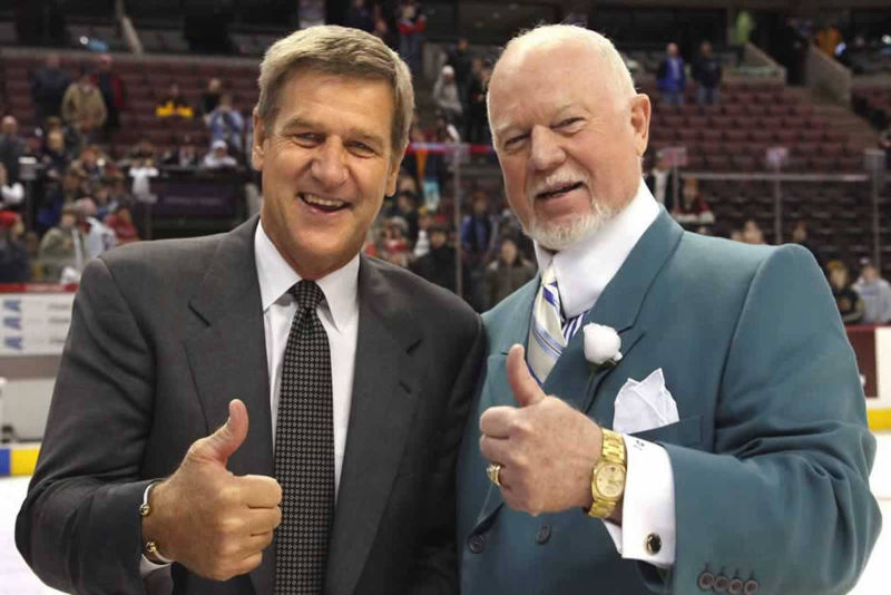 A photo of Don Cherry and Bobby Orr similing with their thumbs up.  They are on the ice of a hockey rink with the bleachers behind them.