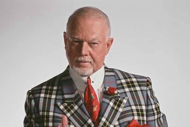 An image of Don Cherry wearing a grey plaid jacket, white high collar dress shirt with a red tie, small red rose on his lapel and a red pocket flash
